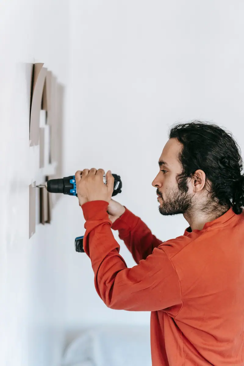 Håndverker i rød genser borer i en lys vegg i et moderne hjem