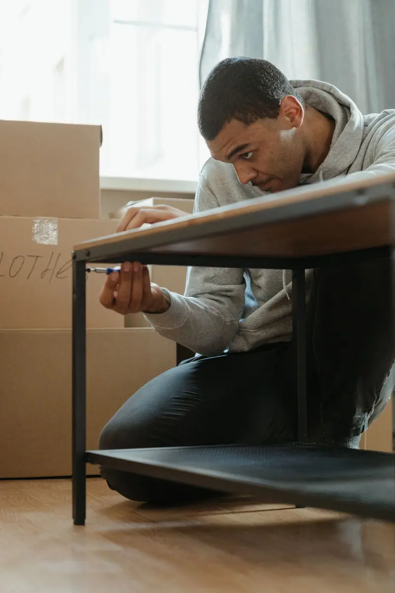 Mann monterer et bord i en ny leilighet med flytteesker i bakgrunnen